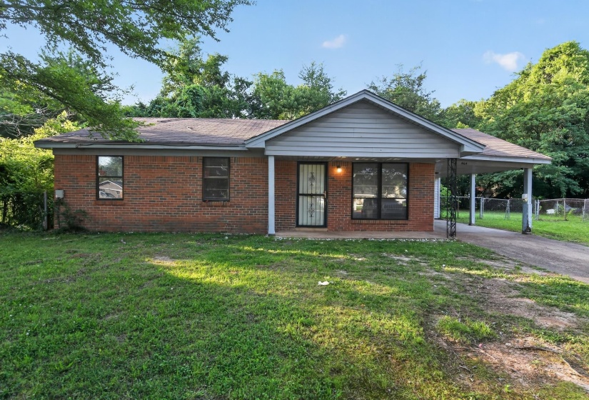 Brick exterior residence with an attached carport, covered front entry, and a gravel driveway
