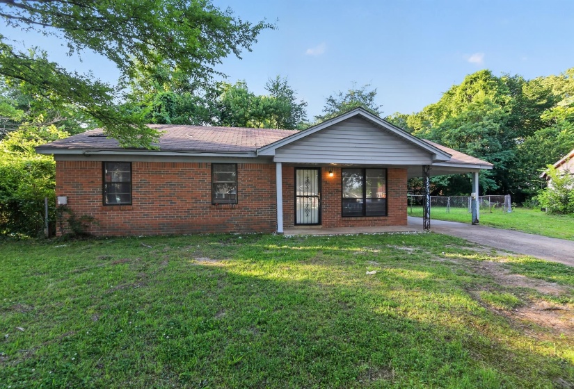 Brick exterior home featuring a covered entryway, attached carport, and a front yard with mature trees
