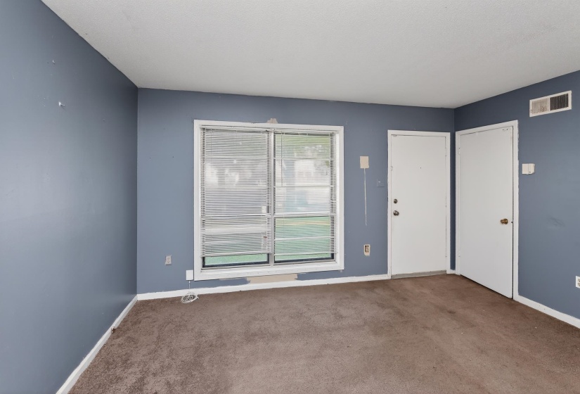 Carpeted room with blue walls, a window featuring blinds, and two white entry doors