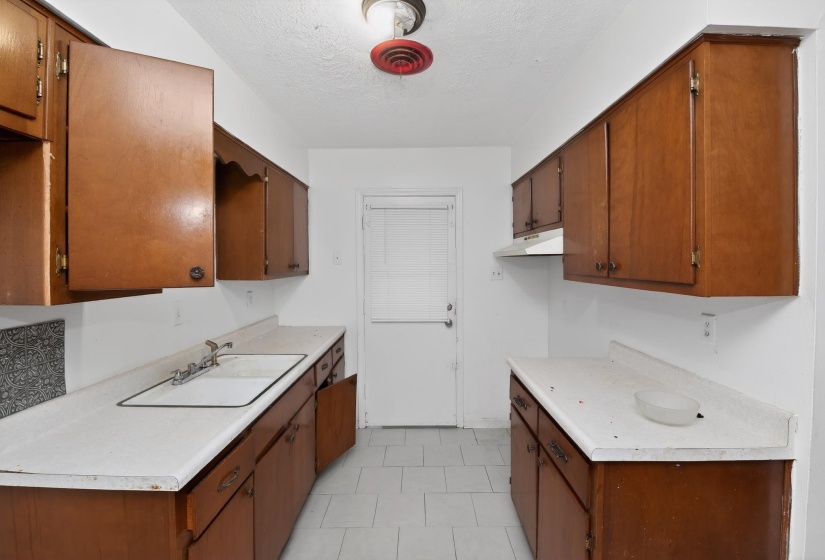 Kitchen featuring wood cabinetry, white countertops, a drop-in sink with a dual-handle faucet, and tiled flooring