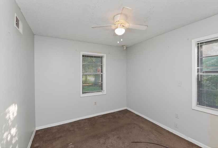 Neutral-toned room featuring a ceiling fan with integrated lighting, two windows with blinds, and brown carpet flooring