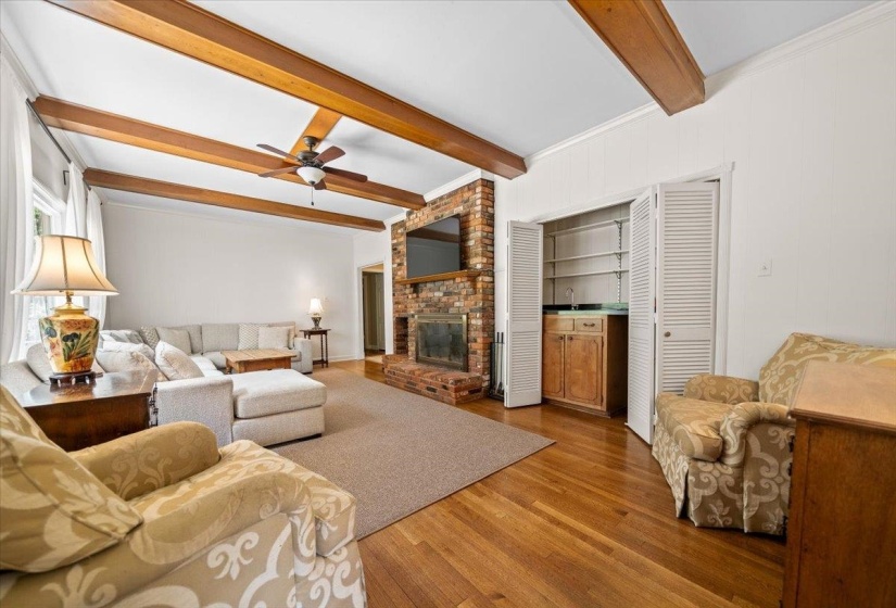 Living area featuring wood-finish flooring, exposed ceiling beams, wet bar and a brick fireplace
