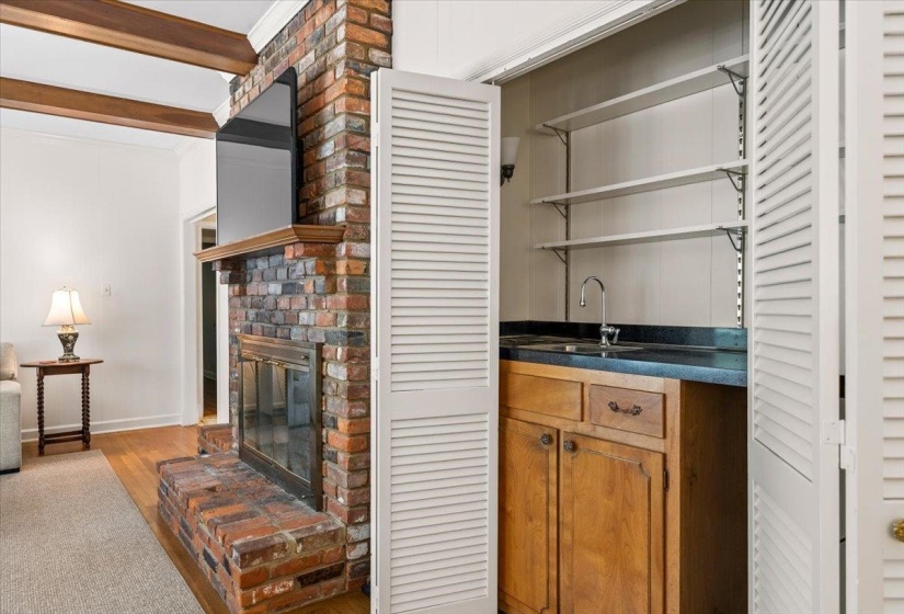 Brick fireplace with a wooden mantel and a built-in wet bar featuring a dark countertop, stainless steel sink, and wood cabinetry, all concealed by louvered bi-fold doors