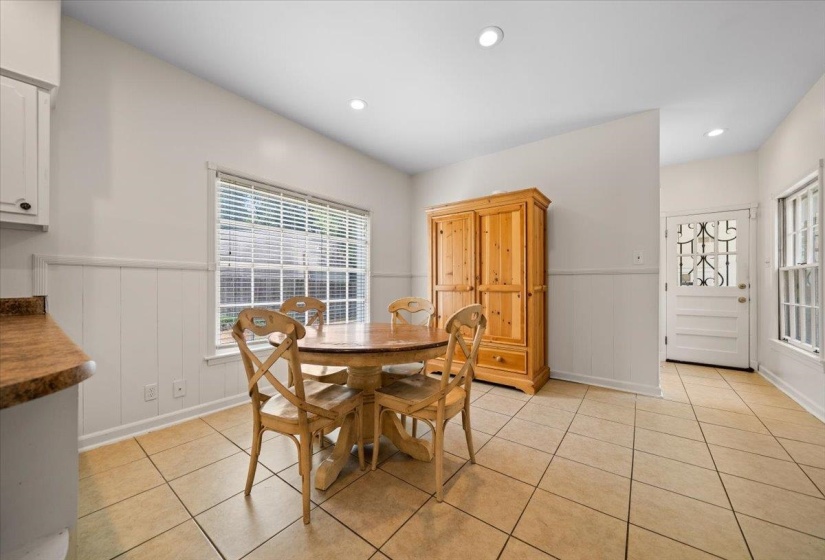 Spacious dining area featuring neutral tile flooring, recessed lighting, a large window with blinds, and wainscoting