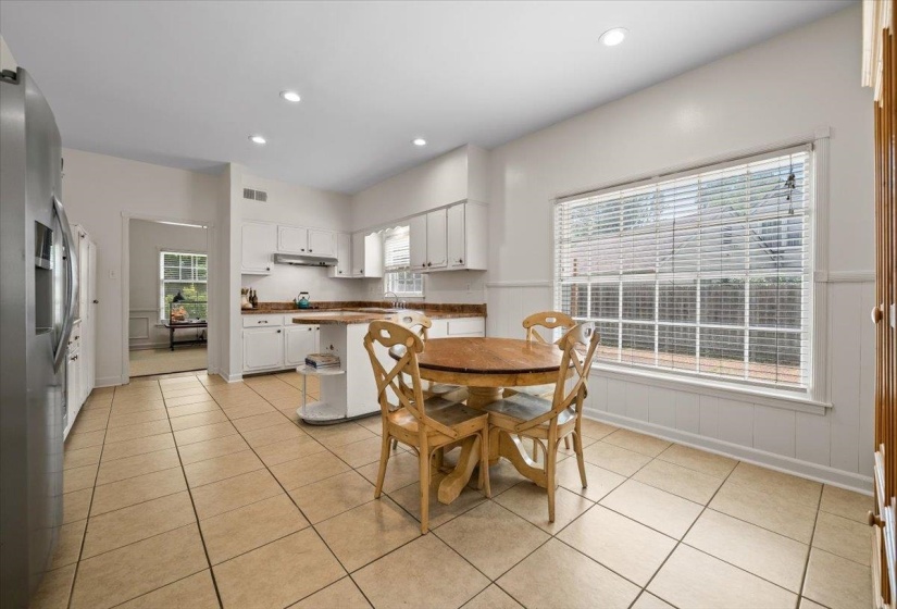 Kitchen featuring tile flooring, white cabinetry, a built-in kitchen island with a countertop extension, and a large window with horizontal blinds