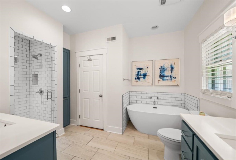 Stunning updated primary bathroom featuring a freestanding soaking tub, a frameless glass shower with subway tile surround, dual vanity sinks with white countertops, and light-toned tile flooring