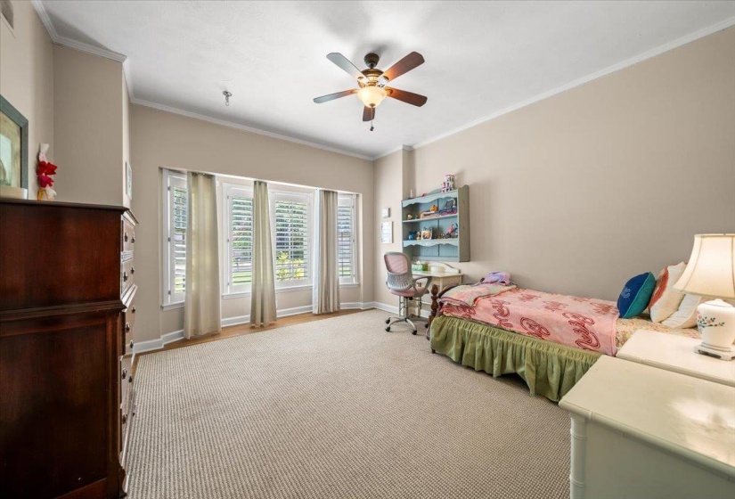 Spacious room with a neutral color palette, featuring a ceiling fan, recessed lighting, and a multi-pane window array with plantation shutters