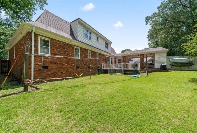 Spacious backyard featuring a manicured lawn, brick facade, white siding, a covered patio, and an elevated deck with white railing