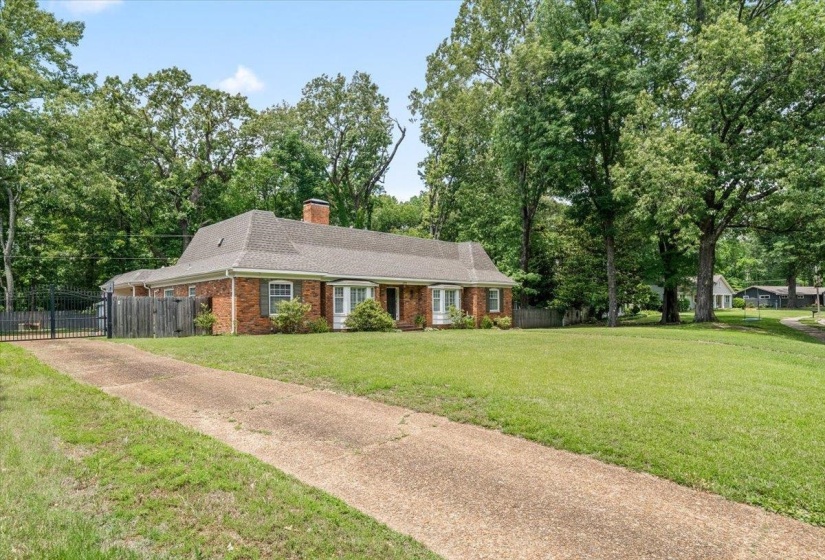 Brick exterior residence featuring a gabled roof, bay windows, and a prominent chimney; electric iron gate