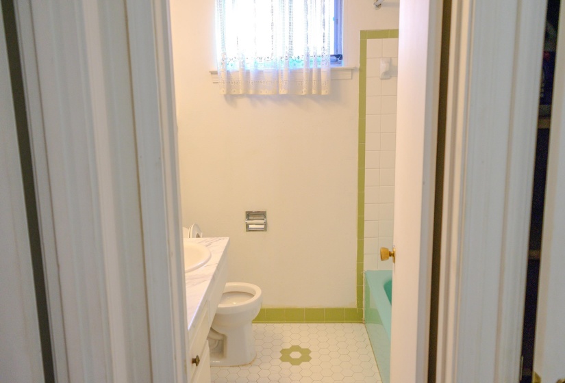 Bathroom featuring a white vanity with integrated sink, white hexagonal floor tiles, and a green bathtub