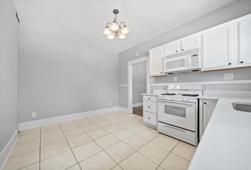 Kitchen featuring white cabinetry, white countertops, a white gas range with an overhead microwave, and beige tile flooring