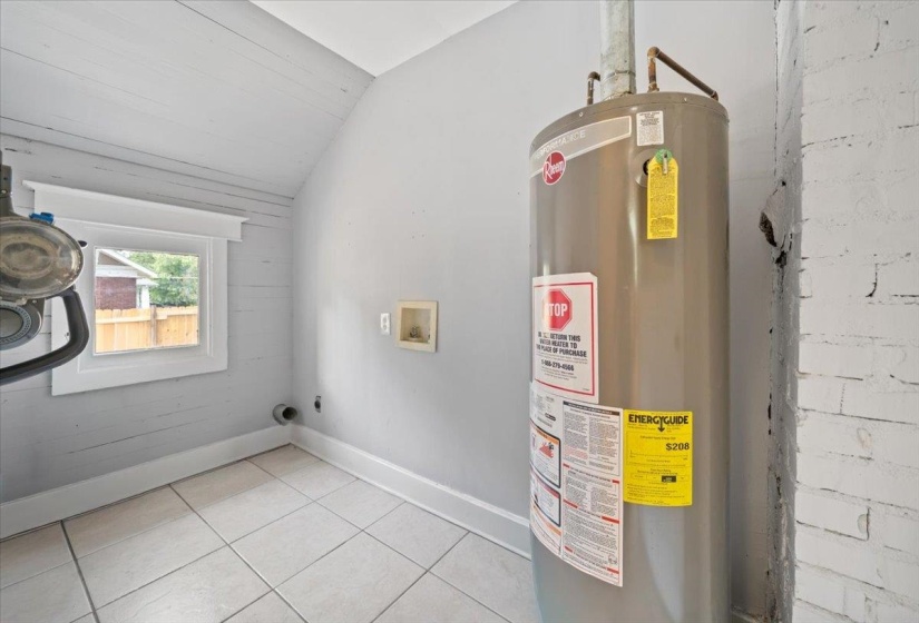 Utility area featuring a water heater, ceramic tile flooring, and a window with white trim