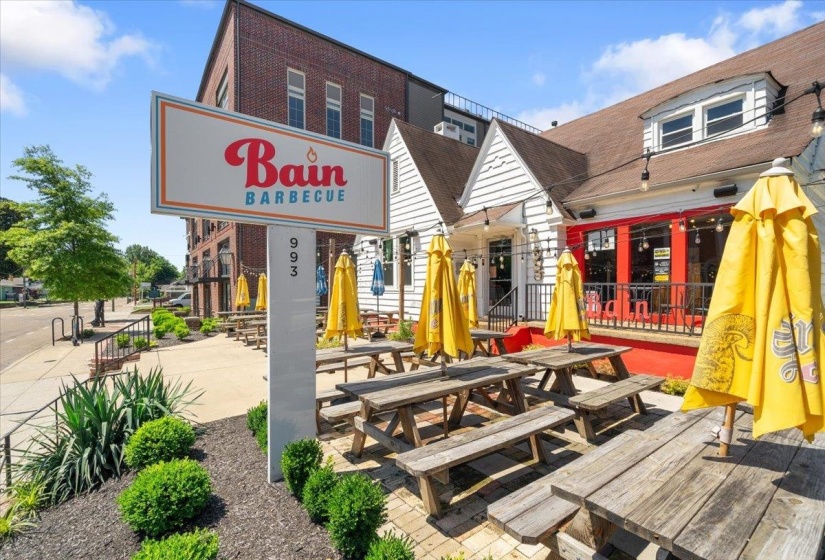 Commercial building featuring a prominent street-facing sign, an inviting outdoor seating area, and a red storefront with large windows