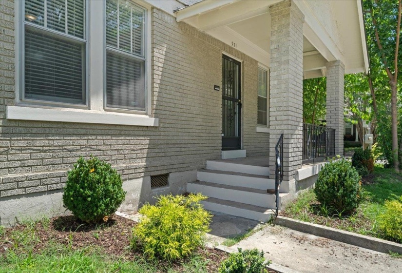 Brick facade with a covered porch featuring brick pillars and black wrought iron railings