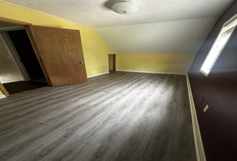 Additional living space featuring wood finished floors, lofted ceiling, a textured ceiling, and baseboards