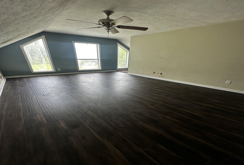 Empty room with a textured ceiling, dark wood-type flooring, lofted ceiling, a ceiling fan, and baseboards