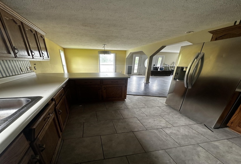 Kitchen featuring stainless steel fridge with ice dispenser, arched walkways, a peninsula, a sink, and a textured ceiling