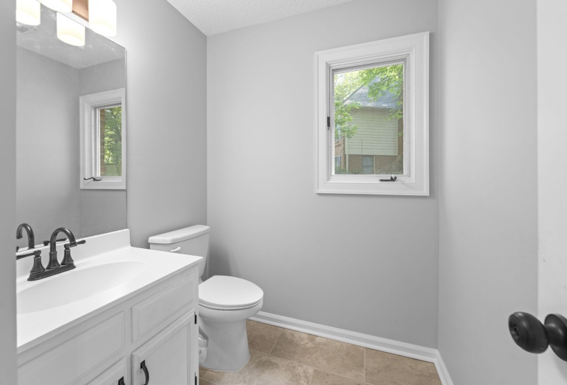 Bathroom featuring a single vanity with a white countertop and dark bronze faucet, a white toilet, and a window with white trim