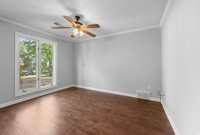 Spacious room featuring wood-finish flooring, light grey walls, and white crown molding