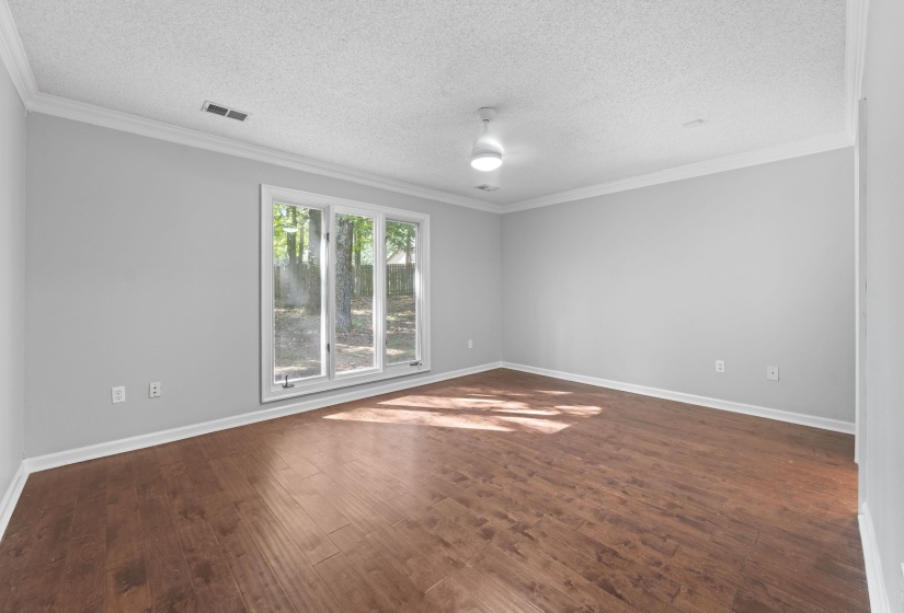 Hardwood-finish flooring highlights this room featuring a large three-panel window, light gray walls, white crown molding, and a ceiling-mounted light fixture