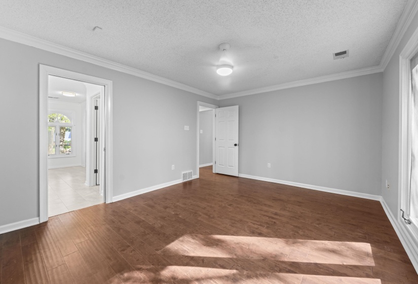 Spacious interior room featuring wood-finish flooring, light gray walls, white crown molding, and a ceiling-mounted light fixture
