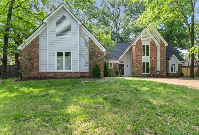 Brick and siding exterior featuring gabled rooflines, a front entry, multiple window styles, and mature trees