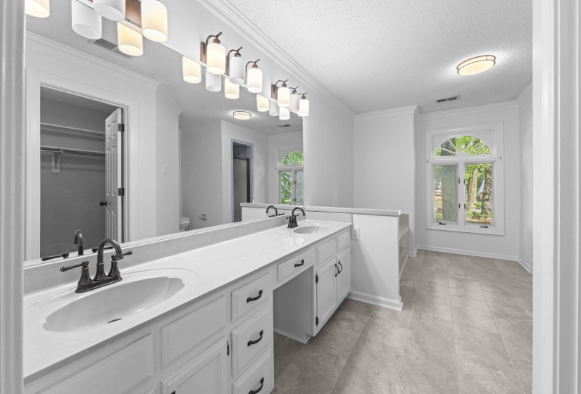 Expansive bathroom featuring a double vanity with white cabinetry, a large integrated mirror, and dual bronze-finish faucets