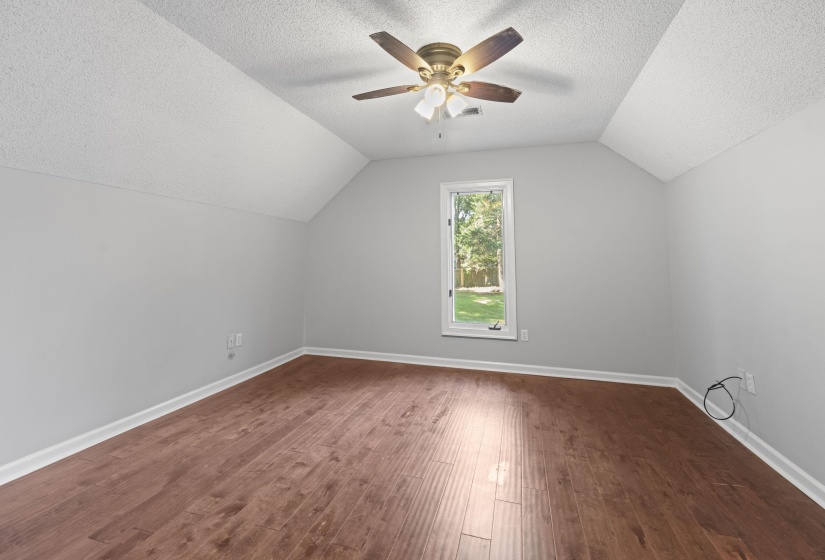 Attic room featuring wood-finish flooring, a single window, and sloped ceilings