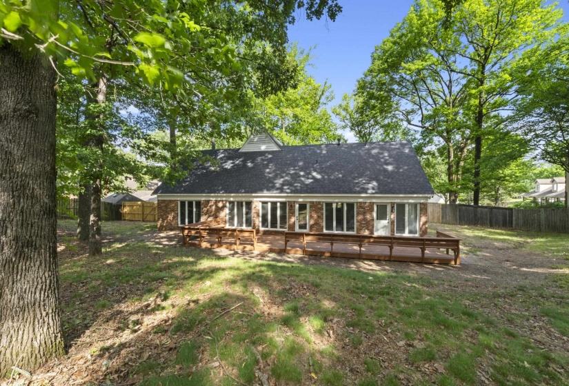 Expansive backyard featuring a multi-level wooden deck, a brick facade, numerous windows, and a mature tree canopy