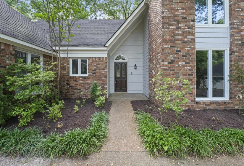 Brick and siding exterior featuring a dark wood arched entry door with transom window
