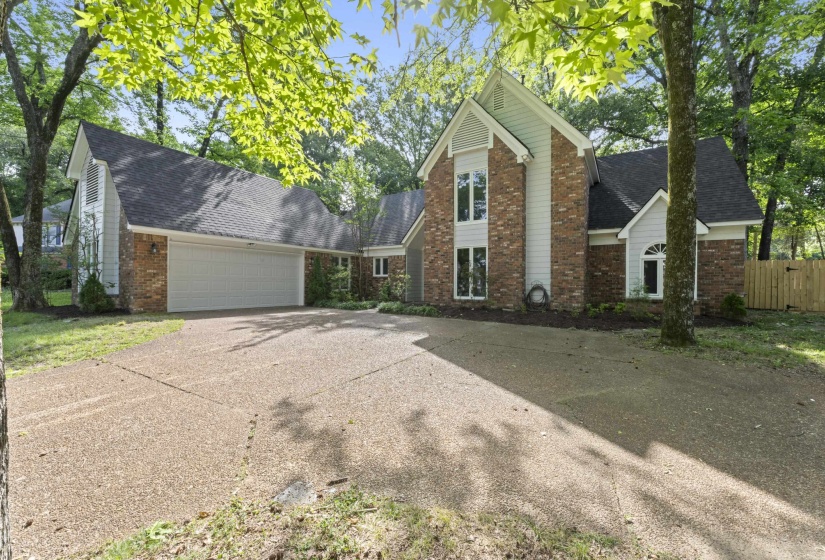 Brick and siding exterior featuring a multi-gabled roofline, a two-car garage, an exposed aggregate driveway, and mature landscaping