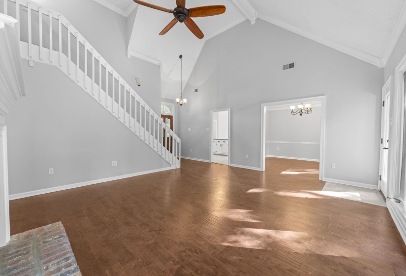Spacious living area featuring wood-finish flooring, vaulted ceilings, and a ceiling fan with integrated lighting