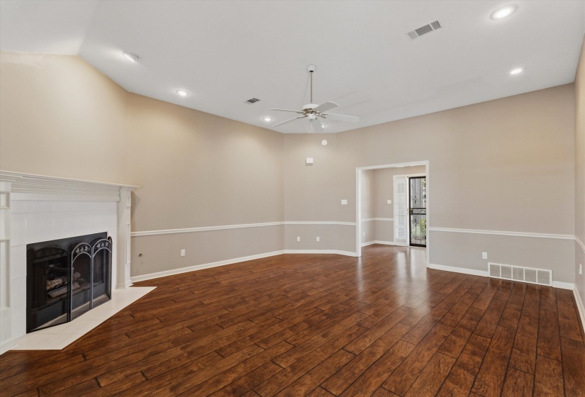 Spacious living area featuring wood-finish flooring, a white mantel fireplace, vaulted ceilings, and recessed lighting