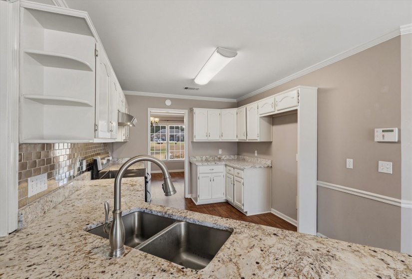 Kitchen featuring a double basin stainless steel sink with a high-arc faucet, granite countertops, white cabinetry, and a metallic tile backsplash