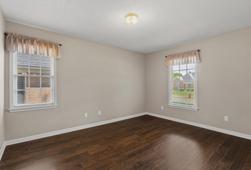 Room featuring dark wood-finish flooring, light-toned walls, and two double-hung windows with white trim
