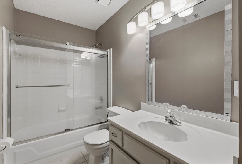 Bathroom featuring a vanity with an integrated sink, a large wall-mounted mirror with a decorative frame, and a tub-shower combination with a sliding glass enclosure