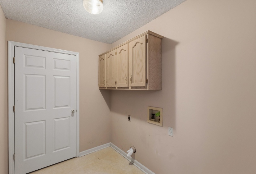 Utility space featuring an overhead cabinet with light wood-finish doors, a neutral wall color, and a textured ceiling