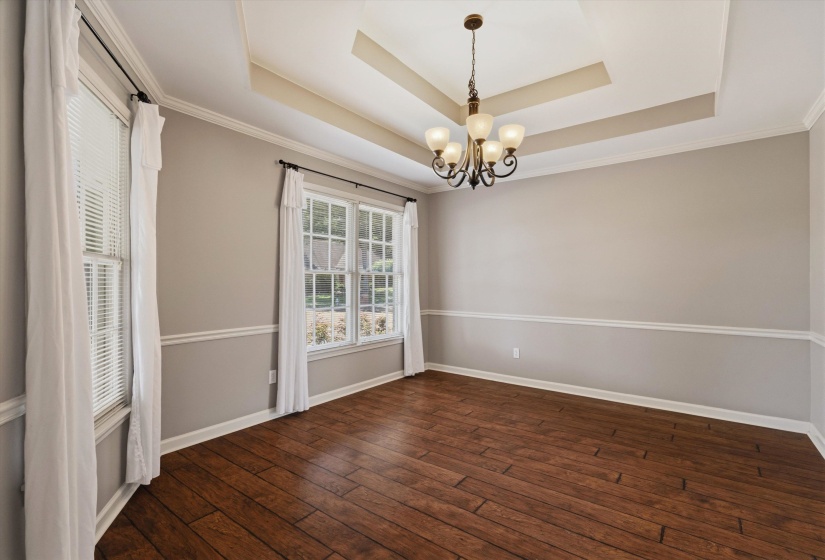 Expansive room featuring wood-finish flooring, a tray ceiling with a chandelier, and multiple windows