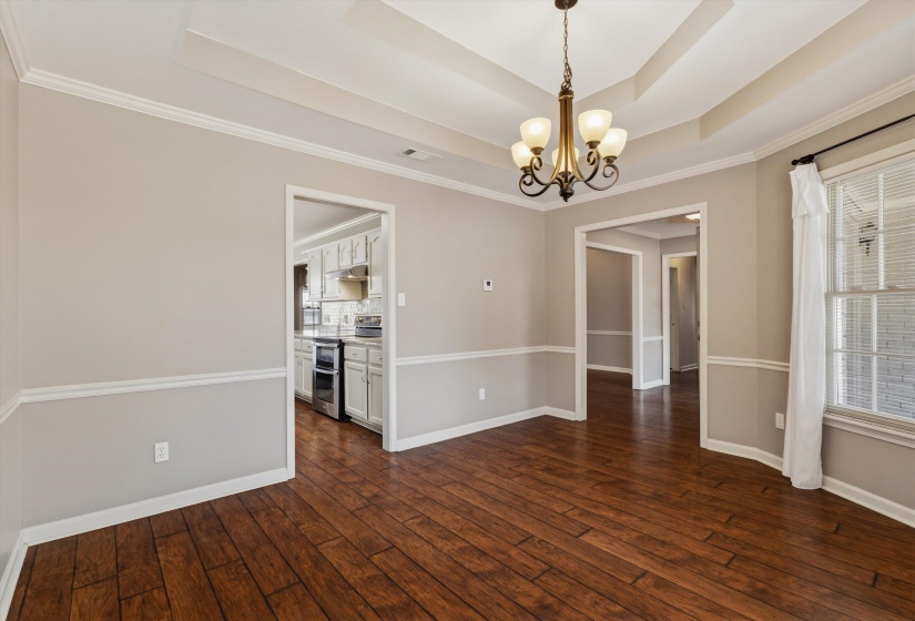 Formal dining area featuring wood-finish flooring, a coffered ceiling with a central chandelier, and wainscoting