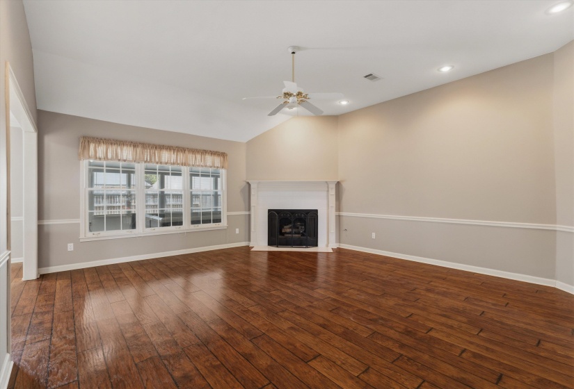 Spacious living area featuring wood-finish flooring, a fireplace with a white mantel, a vaulted ceiling, recessed lighting, and a ceiling fan