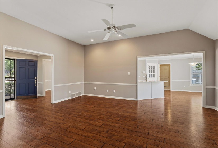 Vaulted ceiling living space featuring wood-finish flooring, two-tone painted walls with chair rail molding, and a white ceiling fan with integrated lighting