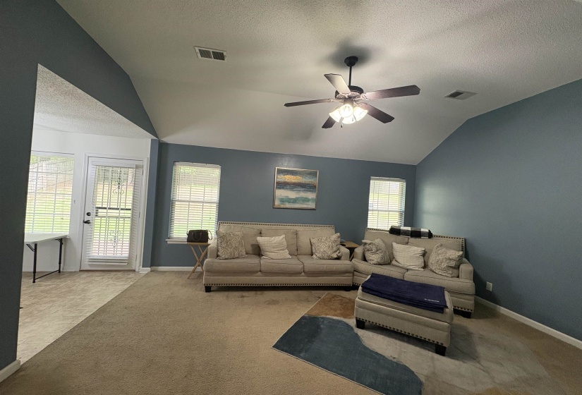 Vaulted ceiling living area with a ceiling fan, multiple windows, and a glass-paneled door