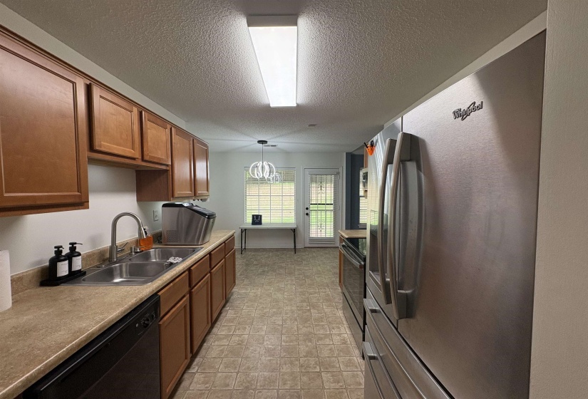 Galley kitchen featuring wood-finish cabinetry, a double basin stainless steel sink with a gooseneck faucet, and a black built-in dishwasher