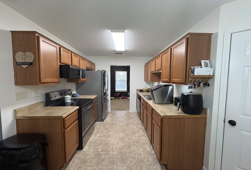 Galley kitchen featuring light wood-finish cabinetry, a black electric range, a built-in microwave, and stainless steel refrigerator