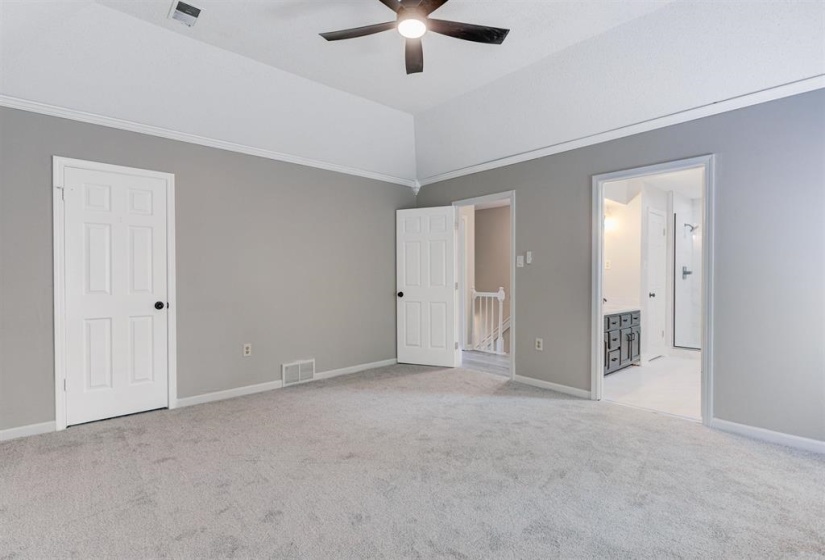 Unfurnished bedroom featuring light carpet, ceiling fan, ensuite bathroom, and vaulted ceiling