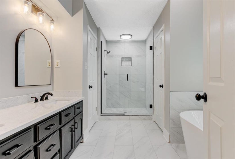 Bathroom featuring a stall shower, double vanity, a freestanding bath, and light marble finish floors