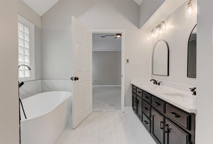 Bathroom featuring double vanity, light marble finish floors, a freestanding bath, and lofted ceiling