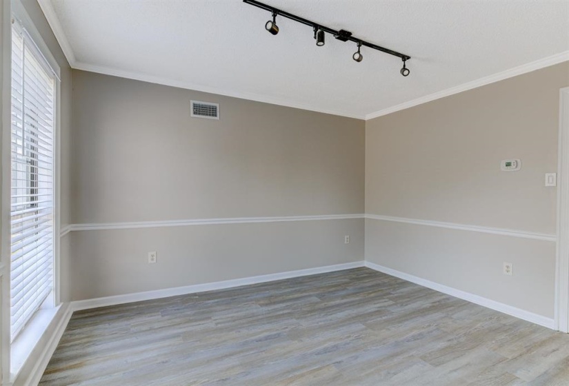 Empty room featuring light wood-type flooring, ornamental molding, and track lighting