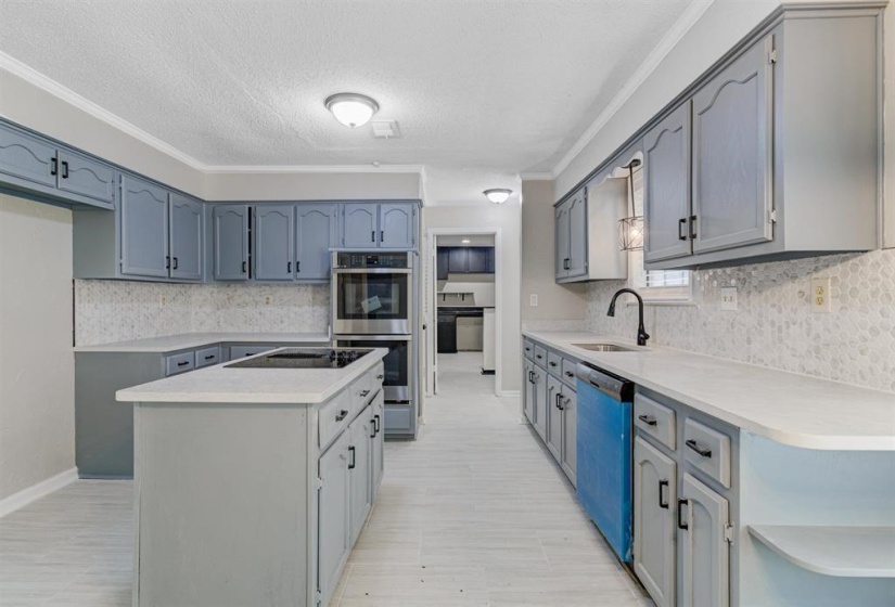 Kitchen featuring decorative backsplash, stainless steel double oven, a kitchen island, a textured ceiling, and dishwasher