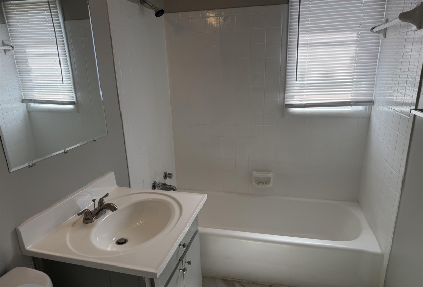 Bathroom featuring a white bathtub with subway tile surround, single vanity with integrated sink, chrome faucet, and a wall-mounted mirror